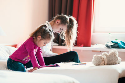 Girl watching video in digital tablet by sister on bed at home