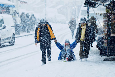 Full length of friends pulling woman on snow covered road
