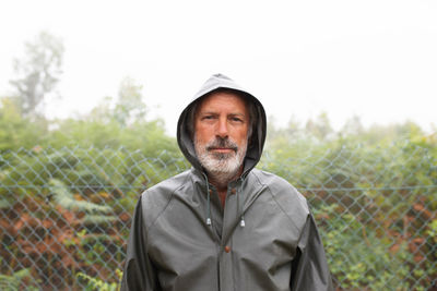 Front view of person in jacket with hood standing on footpath near grassy field and tall tree in misty weather person