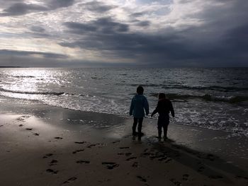 People walking on beach against sky during sunset