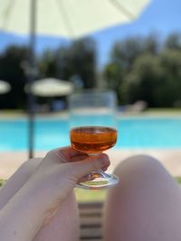 Midsection of man holding wineglass by swimming pool