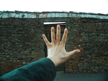 Cropped image of hand against old brick wall