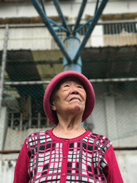 Low angle view of thoughtful senior woman looking away while standing against building