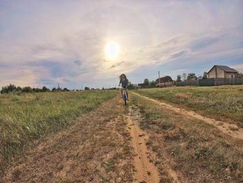 Girl riding bicycle on field against cloudy sky during sunset