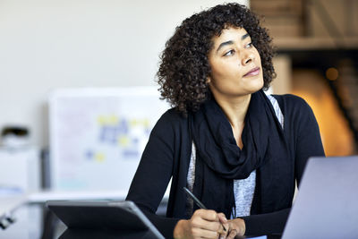 Thoughtful businesswoman with curly hair looking away while standing at desk in office