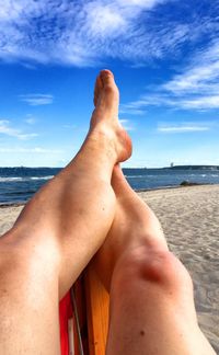 Low section of person relaxing at beach against blue sky during sunny day