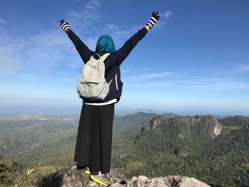 Woman with arms outstretched standing on landscape against sky