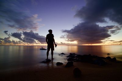 Full length of man standing on rock at beach during sunset