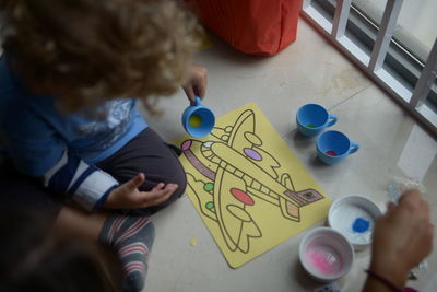 High angle view of kid painting paper while sitting on table