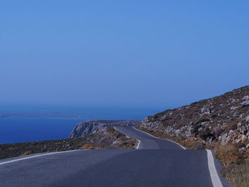 Road by sea against clear blue sky