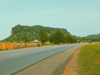 Road leading towards trees against clear blue sky