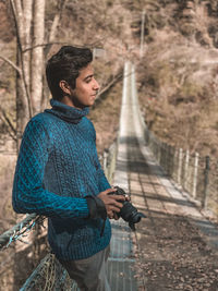 Young man looking away while standing on tree
