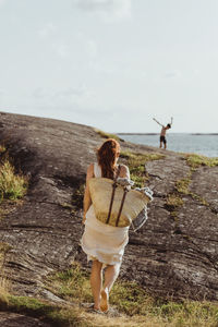 Rear view of woman with bag walking on land against sky during sunny day