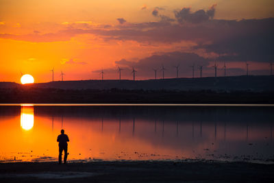 Silhouette man standing on shore against orange sky