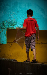 Rear view of boy standing against yellow wall