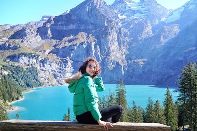 Side view portrait of woman sitting on railing with lake in background against mountains during winter