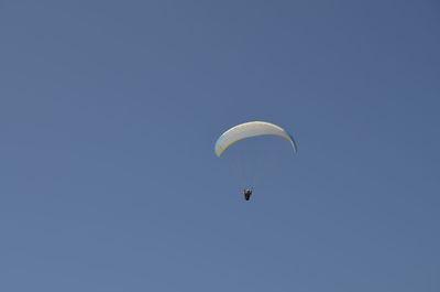 Low angle view of person paragliding against clear blue sky