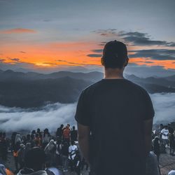 Rear view of people looking at mountains against sky during sunset