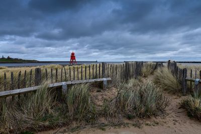 Fence on field against storm clouds