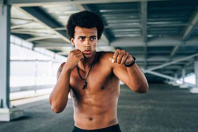 Shirtless male boxer exercising below bridge