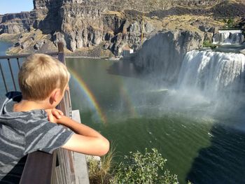 Boy views shoshone falls in idaho, rainbow over water