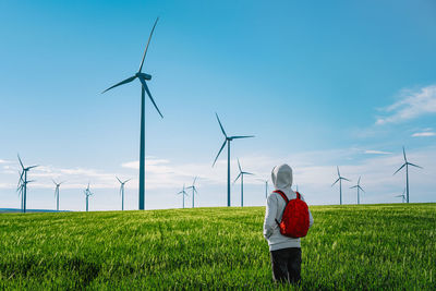 Rear view of man standing by wind turbine on field against sky