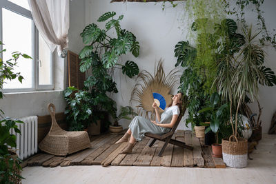 Happy woman florist refreshing in home garden breathing fresh air hold paper fan in hand at hot day