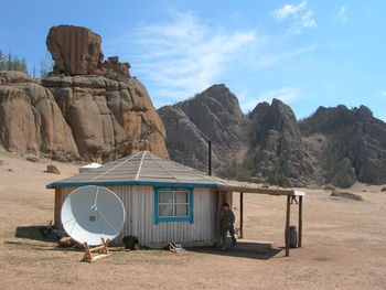 Woman by hut and satellite dish on field against rock formations