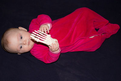 High angle view of baby girl holding bone while lying on black sheet