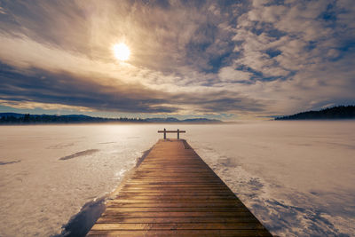 Surface level of pier on beach against sky during sunset