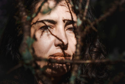 Portrait of a woman looking at camara between  branches in the forest