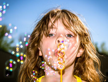 Portrait of girl blowing bubbles against sky