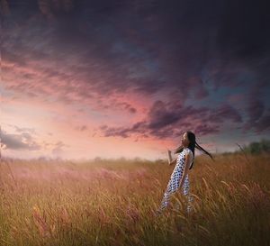 Thoughtful woman walking amidst field against sky during sunset