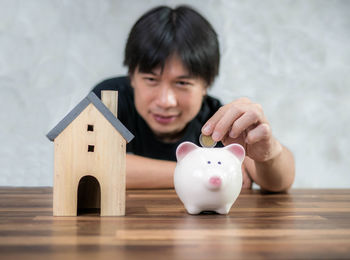 Man putting coin in piggy bank with model house on table