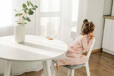 A curious little girl is sitting on a chair in the kitchen. rear view