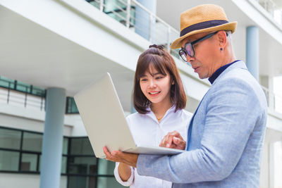 Young woman using mobile phone while standing on laptop