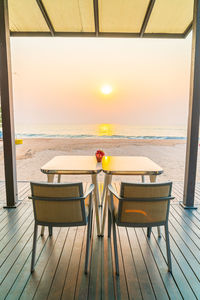 Deck chairs and table on beach against sky during sunset