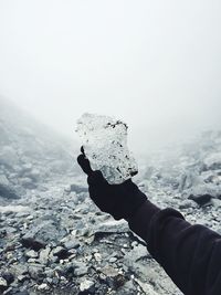 Close-up of hand holding rock in sea against clear sky