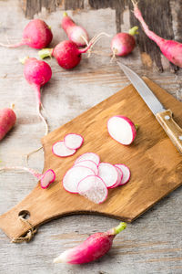 Fresh chopped radishes and a knife on a cutting board on a wooden table