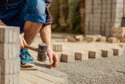 Young man laying gray concrete paving slabs in house courtyard on gravel foundation base. 