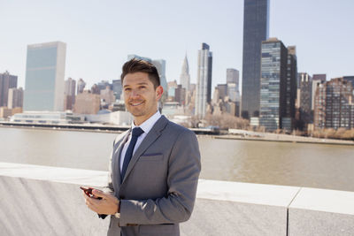 Portrait of a young businessman using his smartphone on a rooftop overlooking the city