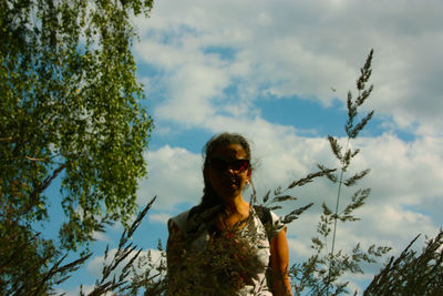 Low angle view of woman standing by tree against sky