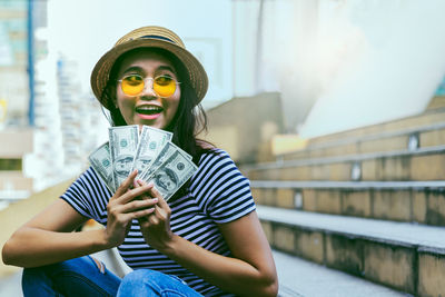 Portrait of woman holding hat sitting against built structure