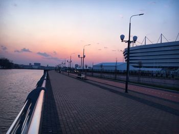 Street by footpath against sky during sunset