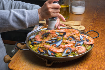 Person seasoning a paella with prawns and mussels, evoking home cooking, typical spanish cuisine,