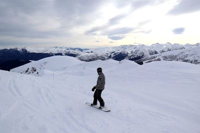 Rear view of snowboarder on snowcapped mountain against sky