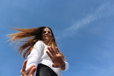 Low angle portrait of woman standing against blue sky