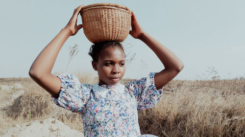 Young woman wearinga dress carrying a traditional pot standing on field against clear sky