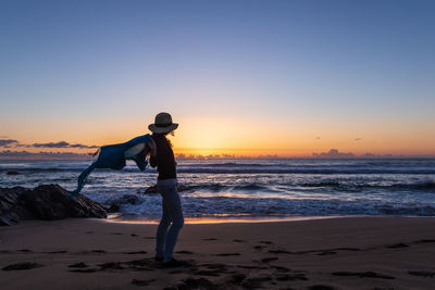 Rear view of man standing at beach against clear sky during sunset