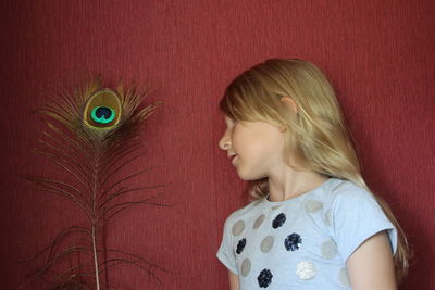 Close-up of girl with peacock feather by red wall